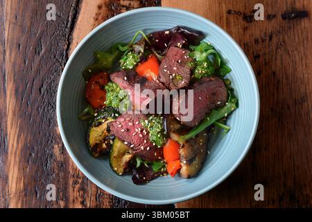 Bowl with warm sliced roast beef and grilled vegetables salad on wooden table Stock Photo