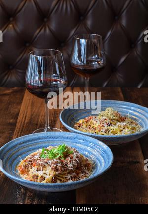 Two bowls of pasta and two glasses of red wine on wooden table Stock Photo