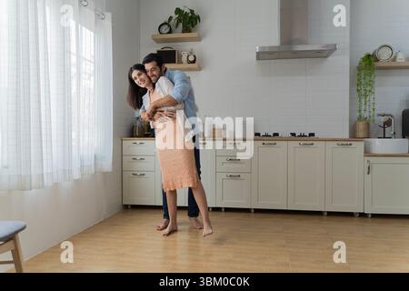 Young couple hugging in modern kitchen with bright window light. Romantic and joyful moment shared in cozy home. Expression of love, connection, and p Stock Photo
