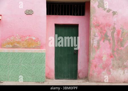 Cuba, Havana. Old Havana wall, peeling pink, green and yellow paint. Green door. (Editorial Use Only) Stock Photo