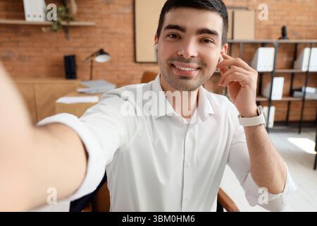 Young man with earphones video chatting in office, closeup Stock Photo