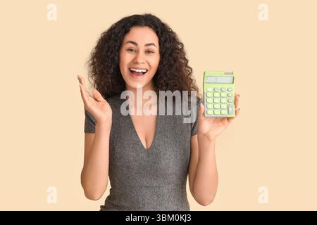 Young African-American woman with calculator on beige background Stock Photo