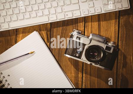Vintage film camera is resting beside keyboard and notebook with pencil in flat design workspace Stock Photo