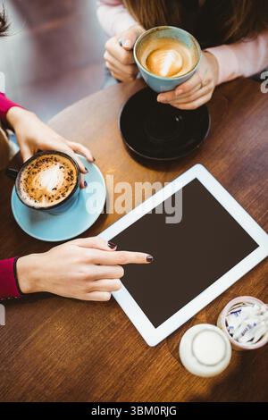Cropped hands of caucasian woman with coffee on table pointing at tablet while talking with friend Stock Photo