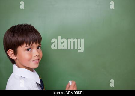 schoolboy is standing in flat design classroom holding white chalk against blank green chalkboard Stock Photo