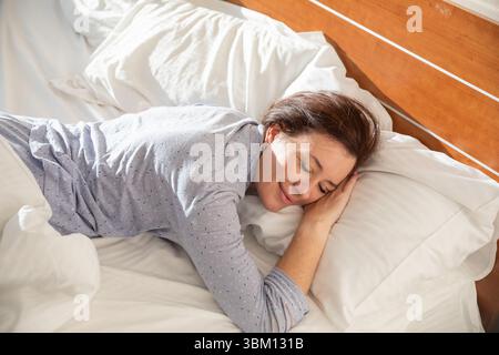 Woman in pajamas sleeping under blanket in the morning in bedroom on bed Stock Photo