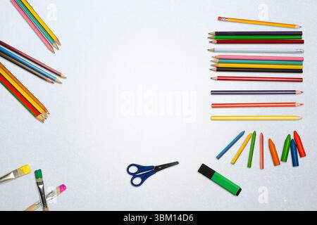Blue-handled scissors are lying on flat design table with pencils, brushes, highlighter, crayons Stock Photo