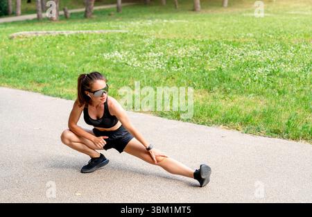 Focused female athlete doing warm up exercise before outdoor workout in city park Stock Photo