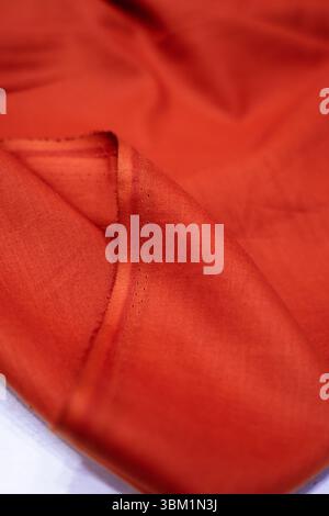 Close-up view of a richly textured, burnt orange fabric. The folds and drapes create a sense of luxury and elegance. The subtle lighting enhances the Stock Photo