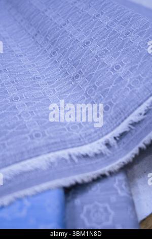 A close-up view reveals the detailed texture of a light blue fabric. The material displays a subtle repeating pattern, characterized by small, circula Stock Photo