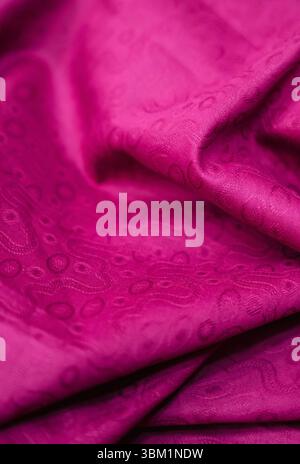 A captivating close-up reveals the intricate details of a magenta fabric, its texture subtly highlighted by soft folds and a delicate, embossed patter Stock Photo