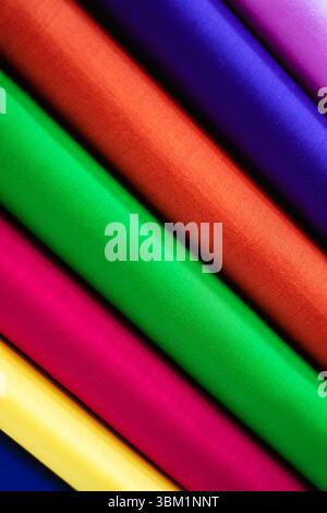 Close-up view of richly saturated fabrics layered diagonally, showcasing a spectrum of intense hues:  deep red, vibrant green, fuchsia pink, sunshine Stock Photo