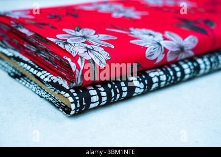 Close-up view of two fabric rolls stacked on a light surface. The top roll features a vibrant red background adorned with a floral print of white and Stock Photo