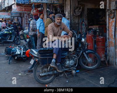 India, Delhi, 25 Jun 2025. Local man sitting on a motorcycle in a busy street of Paharganj, checking his mobile phone. Stock Photo