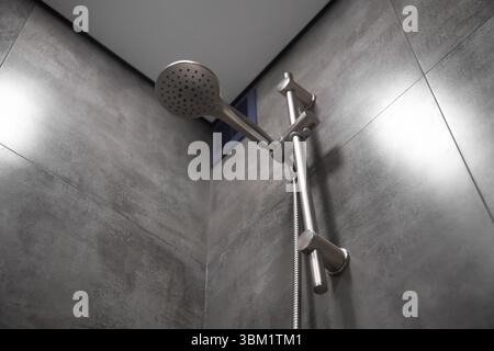 Close-up of a shower head hanging on a rail in a modern bathroom, showcasing sleek design and functionality within a clean and contemporary setting Stock Photo