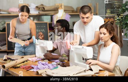 Young male teacher helping students sew while other drawing paper Stock Photo