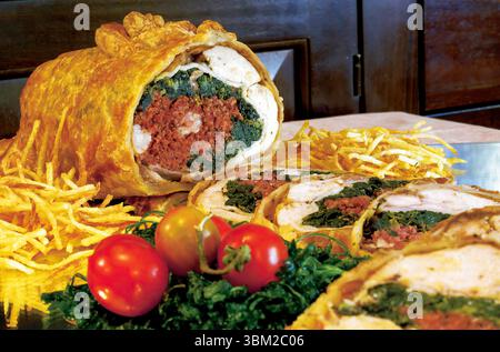 Close up view of a sliced puff pastry stuffed chicken with spinach and speck, garnished with potato straws and cherry tomatoes, served on a tray Stock Photo