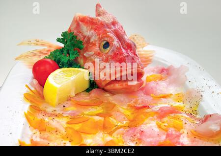 Close up view of a redfish head artfully arranged on a carpaccio dish, enhanced with bottarga, zesty lemon, fresh parsley, ripe tomato, and a sprinkle Stock Photo