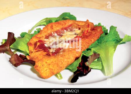 Close up of a delicious breaded cutlet, adorned with crispy bacon and melted cheese, served on a bed of fresh green lettuce, creating a visually appea Stock Photo