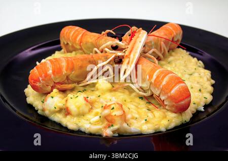 Three cooked Norway lobster tails are elegantly arranged on a creamy risotto, seasoned with parsley, all served on a sophisticated black plate, creati Stock Photo