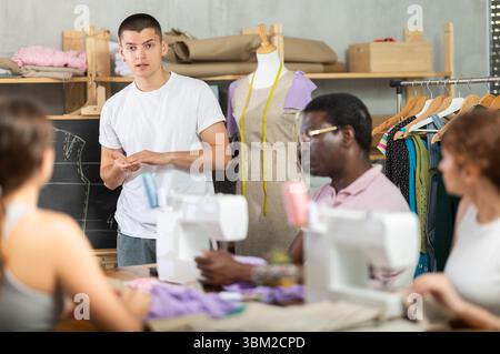 Young sewing instructor guiding adult beginners during practical workshop Stock Photo