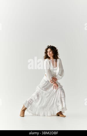 Graceful young woman poses elegantly in a flowing white dress, exuding confidence and style. Stock Photo