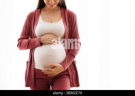 Happy Expectation. Cheerful Pregnant Millennial Woman Touching Her Belly, Standing Against Window Stock Photo