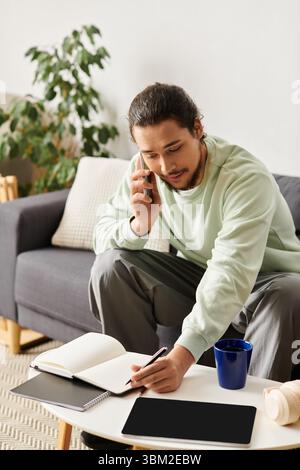A handsome young man sits on the couch, talking on the phone and taking notes. Stock Photo