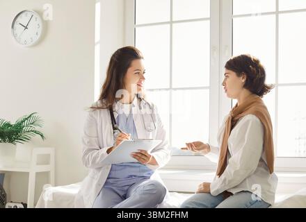 Young woman discussing health concerns with doctor while physician taking notes during consultation. Stock Photo