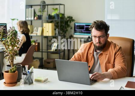Caucasian Young Adult Man Developing Neural Network on Laptop in Office Setting Stock Photo