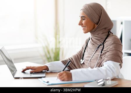 Young female doctor having online training, sitting in her cabinet Stock Photo