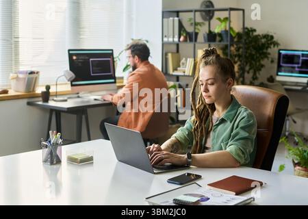 Young Caucasian Woman Developing Neural Network on Laptop in Modern Office Stock Photo