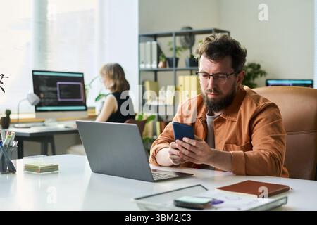 Caucasian Middle Aged Man Developing Neural Network Using Smartphone and Laptop Stock Photo