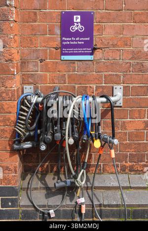 Bicycle locks, cycle locks  hanging fixed to the wall next to bicycle rack in London England United Kingdom UK Stock Photo