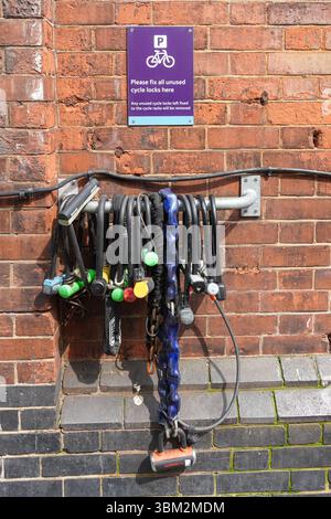 Bicycle locks, cycle locks  hanging fixed to the wall next to bicycle rack in London England United Kingdom UK Stock Photo