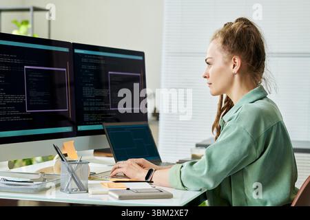 Young Adult Caucasian Woman Debugging Neural Network Code on Dual Monitors Stock Photo