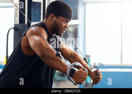 Young black sportsman training triceps on block exerciser in gym Stock Photo