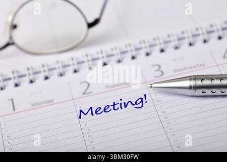 A detailed calendar page with a handwritten meeting reminder, complemented by a pen and glasses. Stock Photo