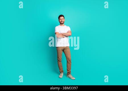 Confident young man standing with arms crossed against a vibrant turquoise background in stylish casual clothing Stock Photo