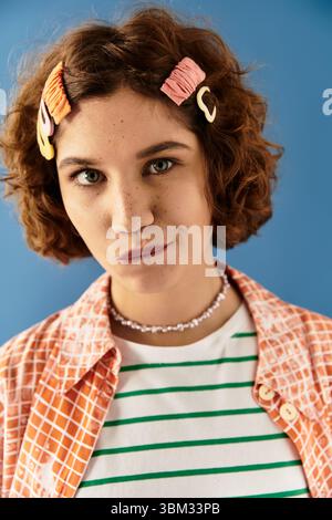 A young woman confidently poses in a colorful outfit with cute hair clips against a blue backdrop. Stock Photo