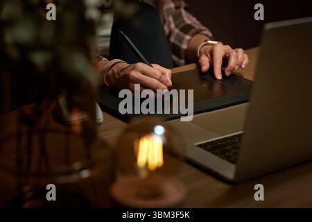 female hands with graphic tablet retouching photo on laptop computer at night Stock Photo