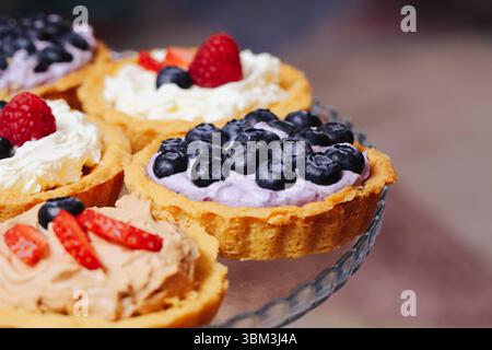 Sweet berry tartlets close up. Mini fruit cakes with cream. Dessert with strawberries blueberries raspberries. Party food idea. Colorful summer treats Stock Photo