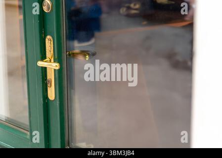 Golden door handle on green frame with glass reflection, ideal for design elements, access visuals, and architectural or security themed content. Stock Photo