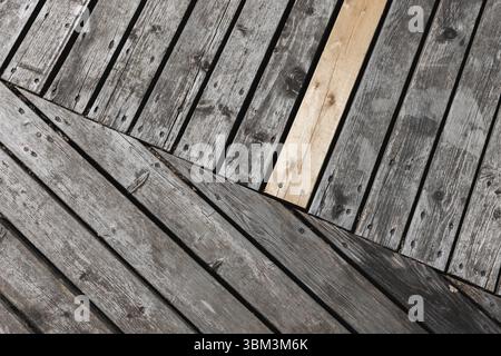 Close-up of weathered wooden planks arranged in a neat geometric pattern, showcasing a contrast between gray aged wood and a single lighter plank, rep Stock Photo