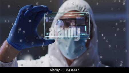 Inspecting man wearing suit, gloves, goggles adjusting digital display in cleanroom, binary data Stock Photo