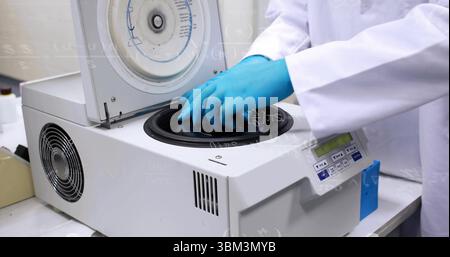 Technician wearing white lab coat loading sample tubes into benchtop centrifuge at lab bench Stock Photo