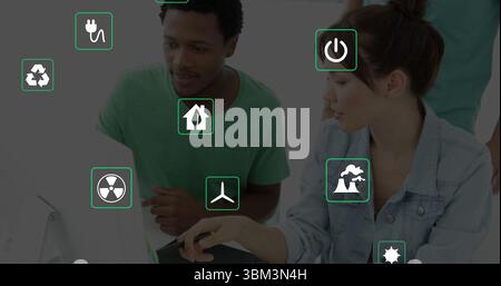 Collaborating adults pointing stylus at laptop screen in office showing floating green energy icons Stock Photo