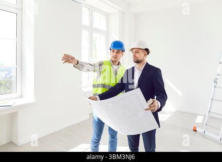 Two men in helmets with a drawing of the building inspect the premises Stock Photo