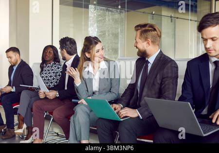 Talking smiling diverse office friendly candidates sitting on chairs in row, business people Stock Photo