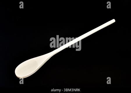 A new wooden spoon with a long handle lies on a black background. Stock Photo